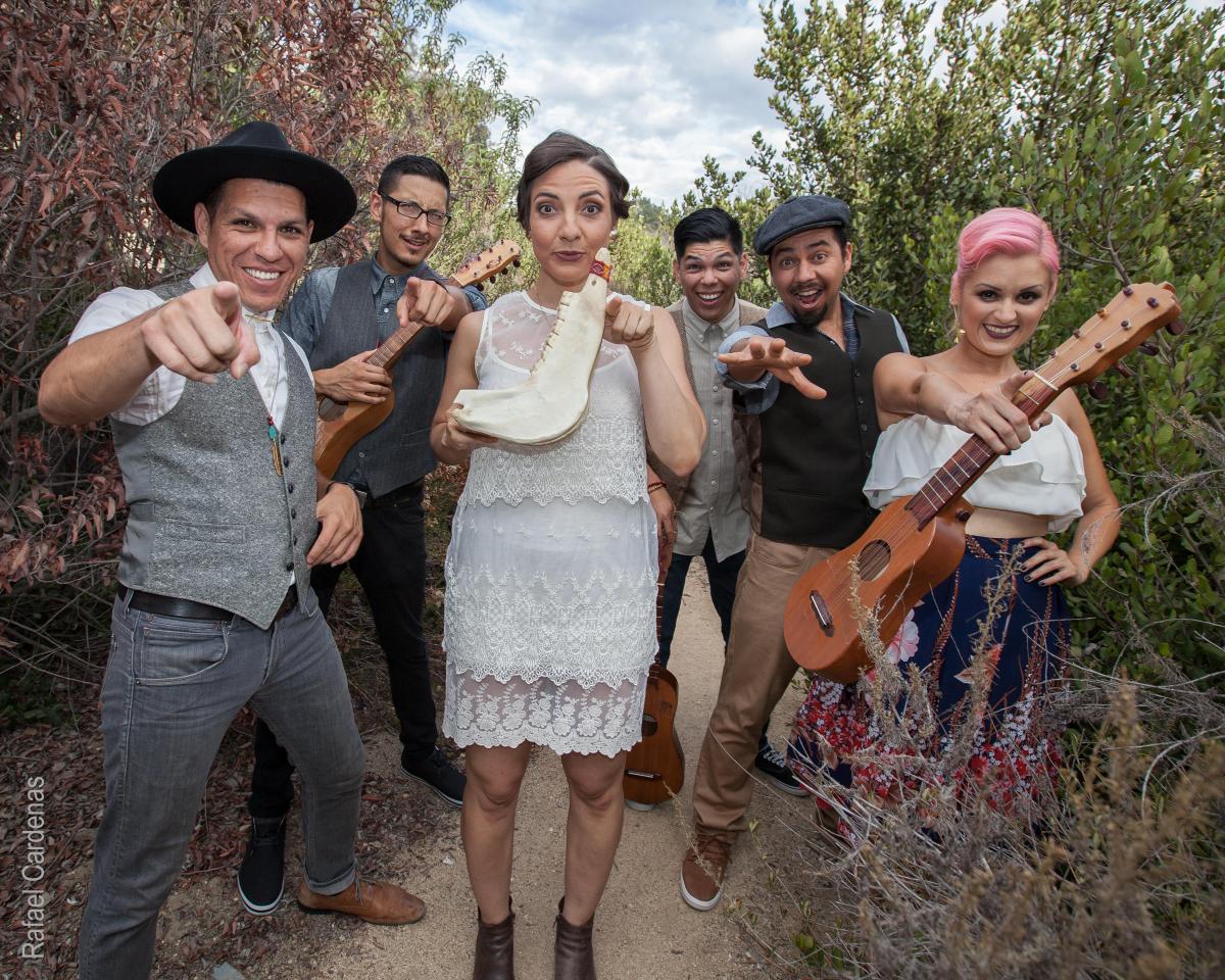 Las Cafeteras musicians point at the camera while holding instruments.