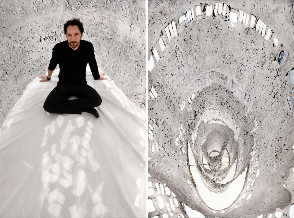 Kevork Mourad sits cross-legged inside a layered sculpture of white fabric and printed ink.