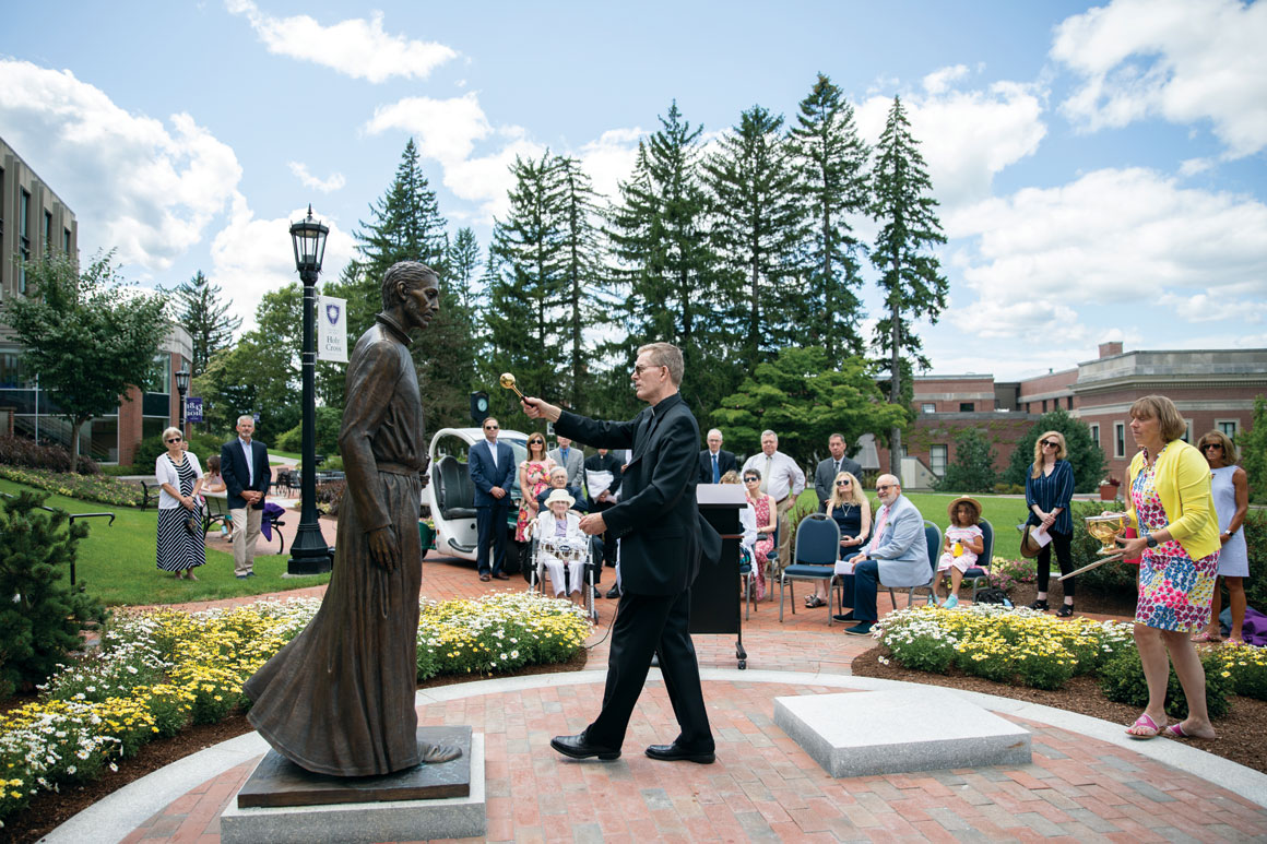 Fr. Boroughs, S.J., blesses a statue of St. Peter Faber in the Hogan Courtyard as guests look on. 