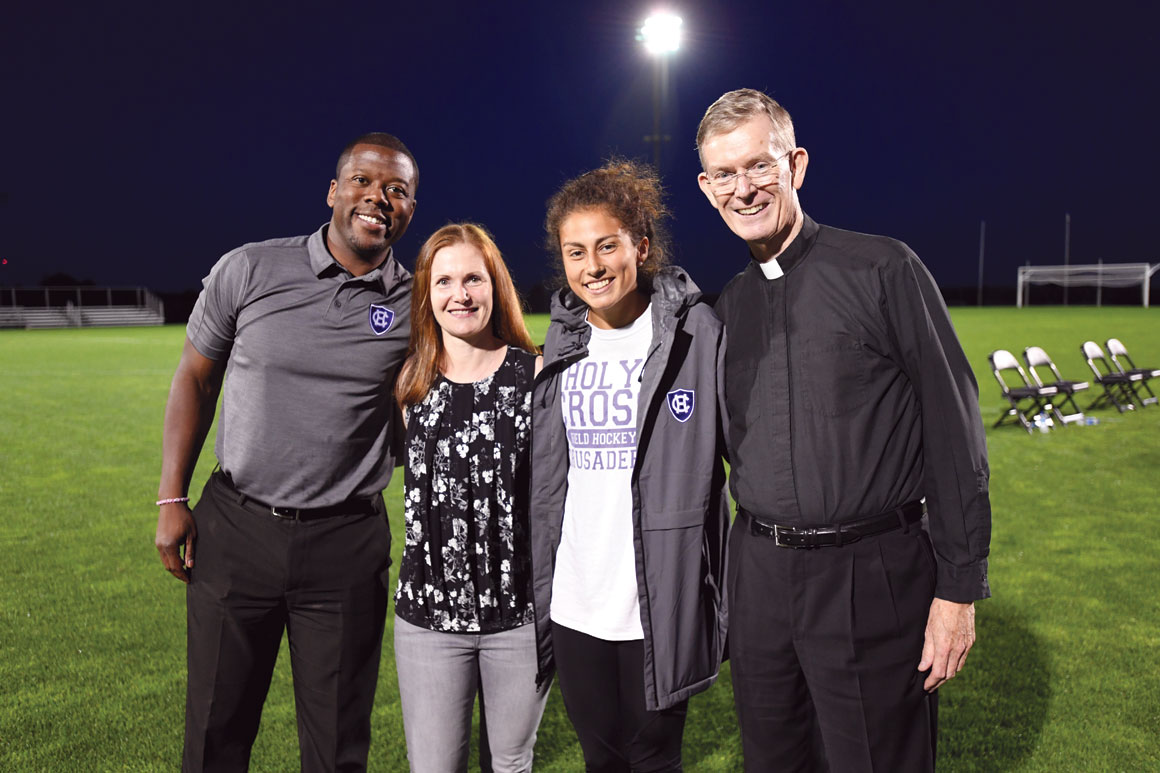 Fr. Boroughs, president of Holy Cross, poses for a photo on a field with Marcus Blossom, director of intercollegiate Athletics, Sarah Petty, faculty Athletics representative and associate professor of chemistry, and Philomena Fitzgerald ’20, Student-Athlete Advisory Committee president and field hockey player. 