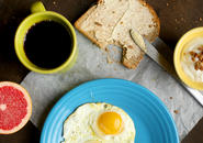 Eggs sunny side up, half a grapefruit, mug filled with coffee, toast with butter, and yogurt with granola.