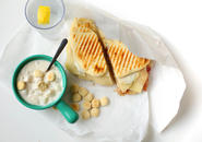 Panini, bowl of clam chowder, oyster crackers, and glass of water with wedge of lemon.