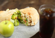 Chicken salad wrap,  green apple and a glass of soda with ice.