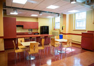 kitchen area in Wheeler Hall with cabinets, refrigerator and sink in the background and tables and chairs in foreground