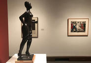 Bronze sculpture of a woman in dress and high heels stepping forward, with print of dancers in background.