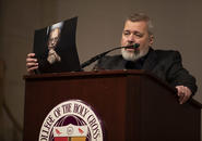 Dmitry Muratov speaks from the podium while holding up a photo of Mikhail Gorbachev, which he later presents to Holy Cross President Vincent Rougeau.