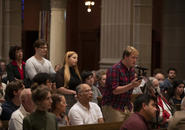 Students and a faculty member form a line at the microphone in the center aisle of the St. Joseph Memorial Chapel, amid hundreds of attendees..