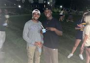 Two students standing outside and smiling at the camera. One student is holding a Gatorade bottle and the other a cup of ice cream while giving the peace sign.