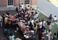 A color photo of a large group of students (a mix of men and women) outside at a cookout. Some people are assembling their plates with hot dogs and hamburgers and some are in little groups talking.