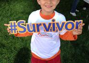 A young boy in a Boston Red Sox Hat is holding a sign that says #Survivor