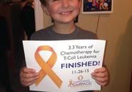 A young boy named Christian holds a sign that says 3.3 Years of Chemotherapy for T-Cell Leukemia on 11/16/2015
