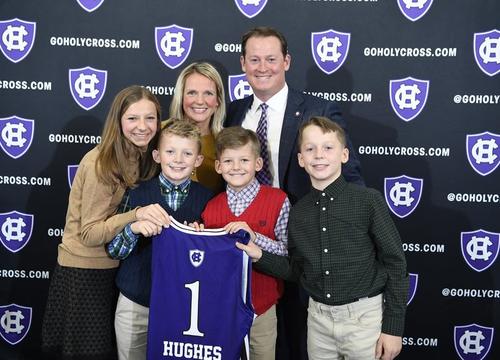 Christopher "Kit" Hughes and his family posing for the camera in front of a Holy Cross athletics background banner.