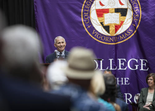 Dr. Fauci speaks in front of a purple Holy Cross backdrop