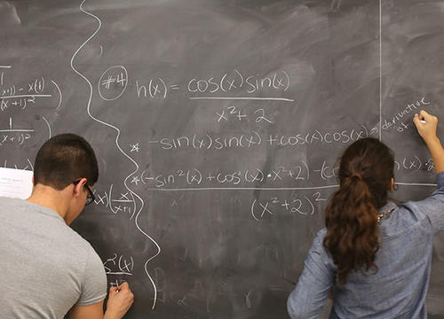 Two students stand at a chalkboard