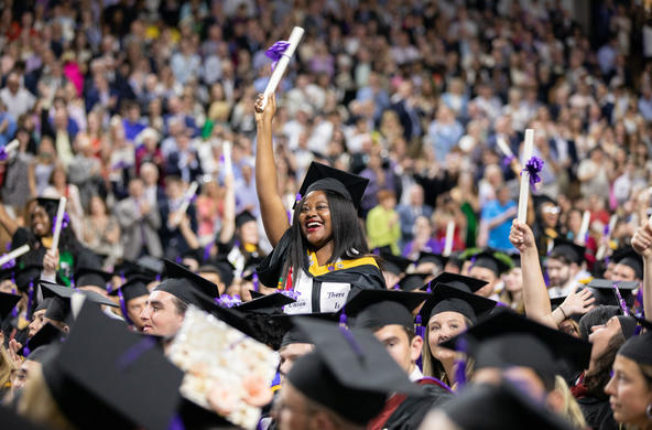 an excited student at Commencement Exercises standing up and holding her diploma up high