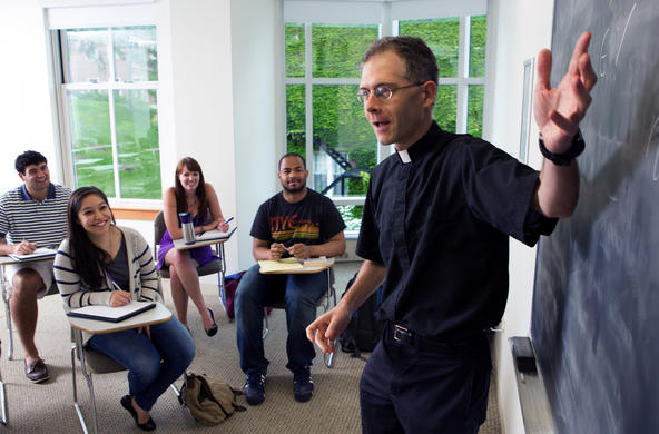 Rev. John Gavin, S.J., professor of religious studies, points to a blackboard before a room full of students