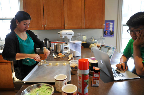 student baking cookies in Campion House, home of the Chaplains' Office, while another another student is on a laptop