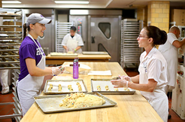 Two dining employees putting cookie dough onto cookie sheets with two other dining employees working in the background