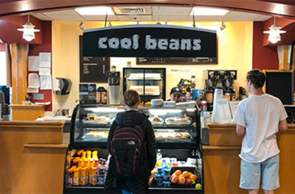 Two students standing in front of the Cool Beans coffee lounge in the Hogan Campus Center.