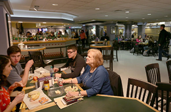A faculty member eating lunch with three students at a table in The Pub.