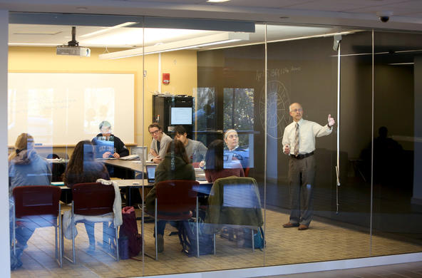 Professor teaching in front of a class as seen through a glass wall.