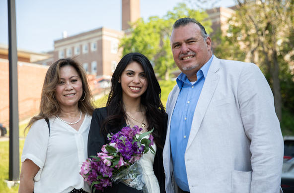 A student holding flowers and flanked by her parents.