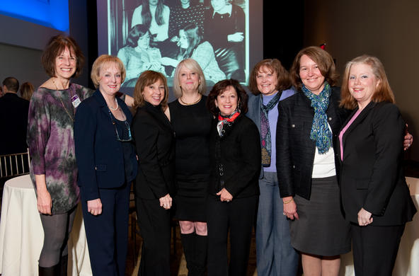 Group of 8 women dressed in business casual posing for a photo an an event inside.