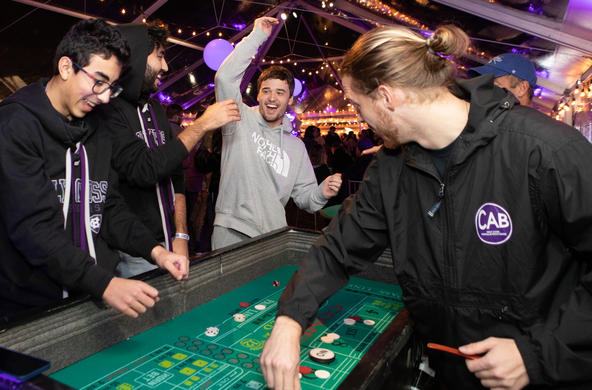 A group of students at a gambling event organized by the Campus Activities Board. Three students are playing a game and a dealer is organizing the board.