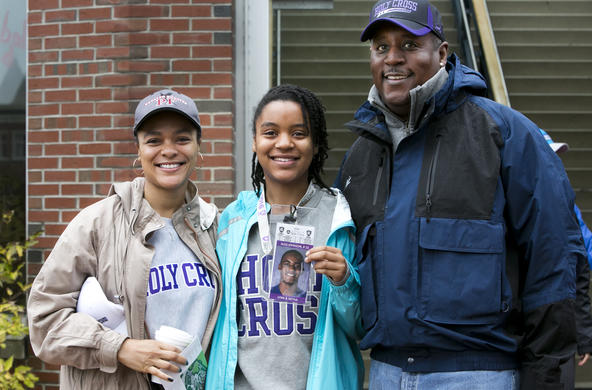 A female student with her parents. Her and her mom are wearing Holy Cross sweatshirts and the dad, a holy Cross baseball hat.