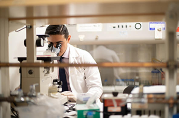 student in a lab coat looking into a microscope
