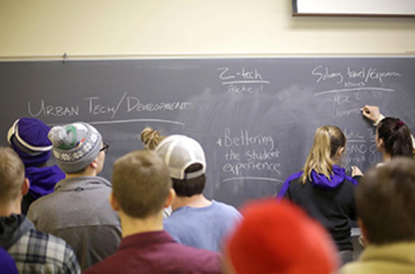 Students and faculty in a classroom at chalkboard 