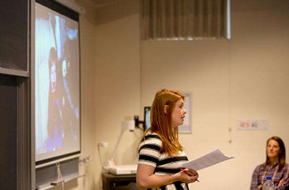 student holding a paper in front of a classroom screen
