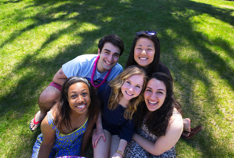 group of five students sitting outside on the lawn looking into the camera