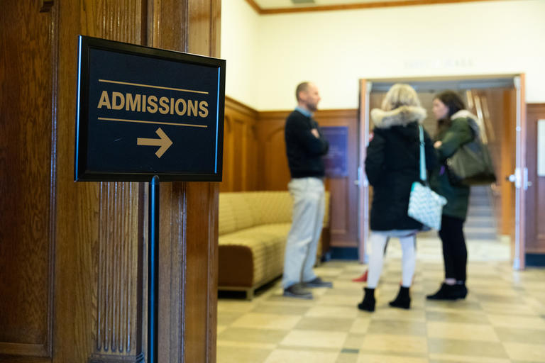 admissions sign in foreground with a group of admissions visitors in the background