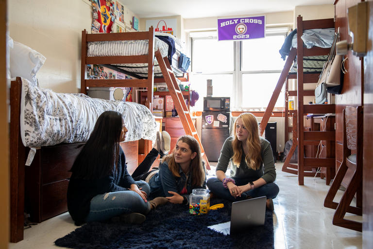 three students sitting on the floor in a residence hall room