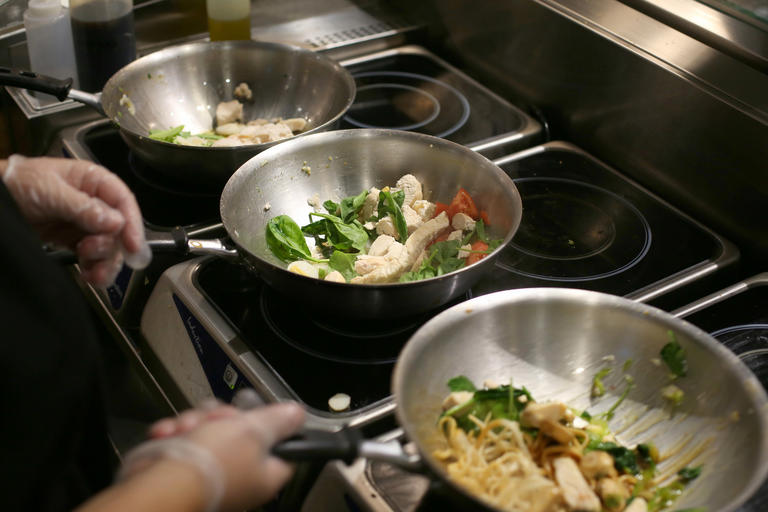 Row of three pans filled with stir fry cooking on burners.