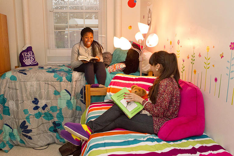 two students sitting on their beds holding books and laughing