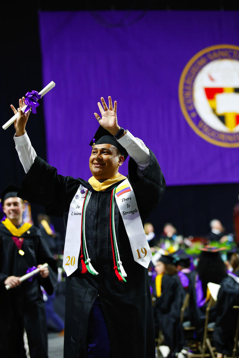 a student at commencement exercises holding his diploma and waving to onlookers