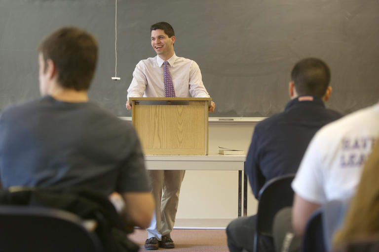 faculty member Eric Fluery stands behind a lectern while teaching his class