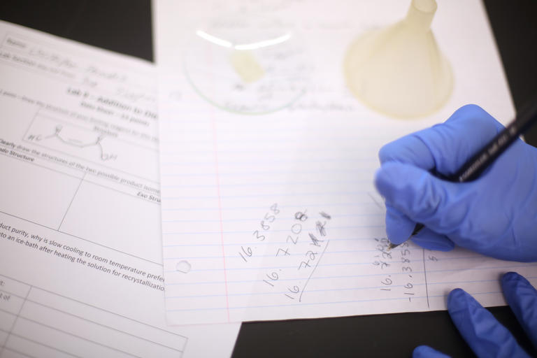 student wearing gloves and taking notes in a science lab