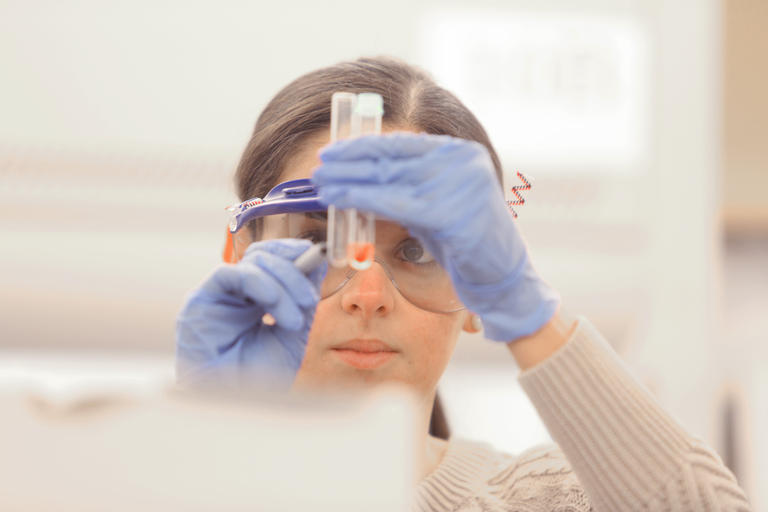 student in a lab wearing goggles and looking at a collection tube