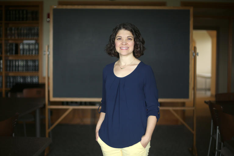 Melissa Boyle, a professor in the economics and account department, stands in front of a chalkboard looking into the camera.
