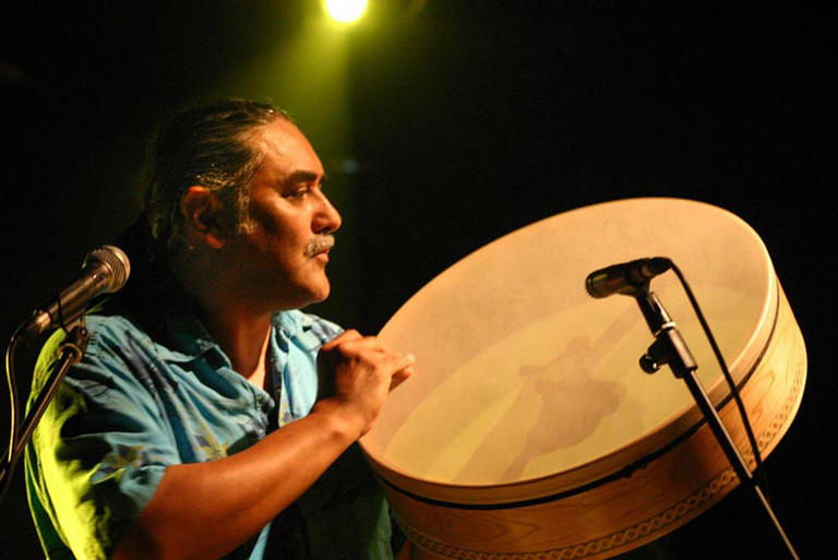 Glen Velez playing a large frame drum in front of a microphone