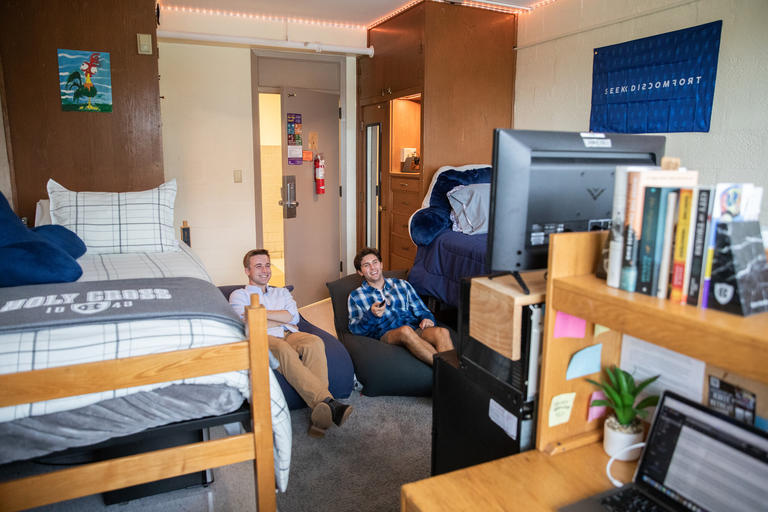 Two students sitting on beanbag chairs watching TV in their residence hall room.
