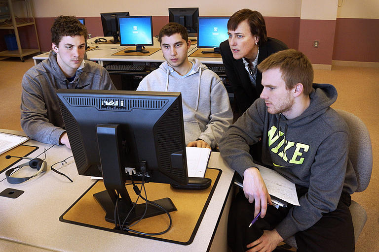 Three students and a professor looking at a computer monitor.