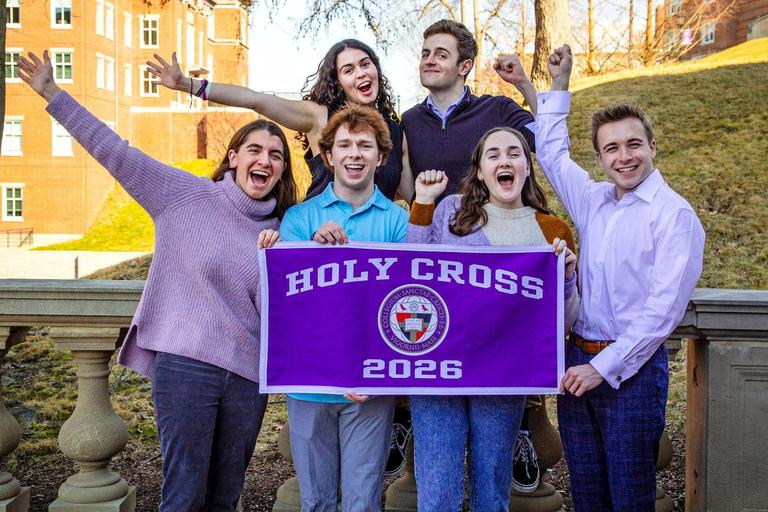 group picture of students both men and women holding a purple holy cross banner