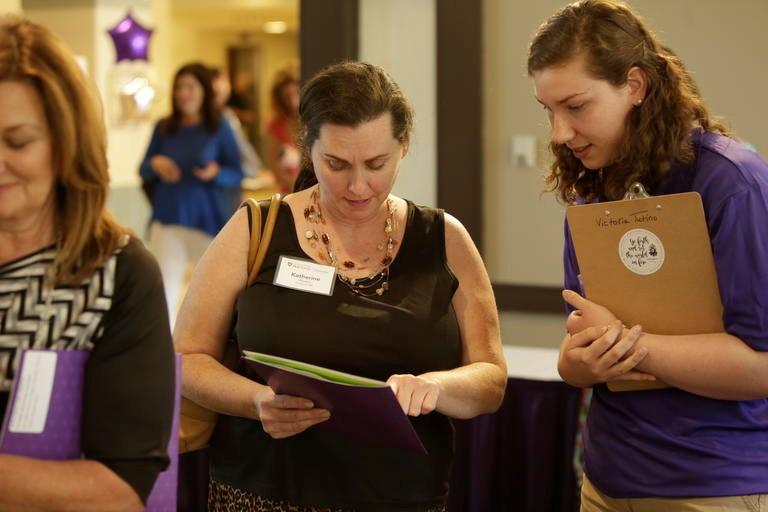 image of student helping a parent at the gateways orientation parent wearing a black top with her hair pulled back, student wearing a purple top holding a clip board