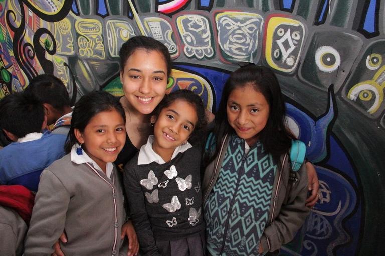 A young lady posting with three young girls. Behind them is a dark, artful wall mural.