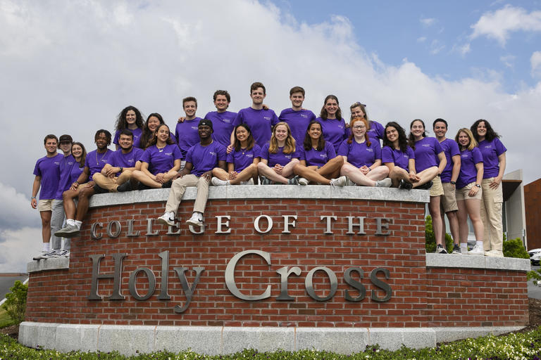 Lots of students wearing purple Holy Cross shirts sitting on the College of the Holy Cross wall.