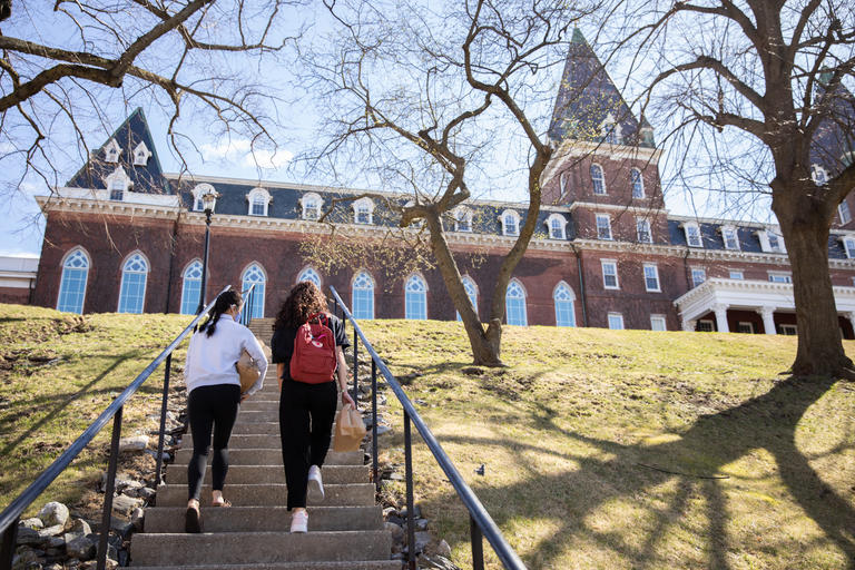 Two students walking up steps outside on their way to Fenwick Hall. The sun is shining on a and early spring day.